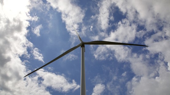 Looking up at the blades of a wind turbine against a blue, cloudy sky
